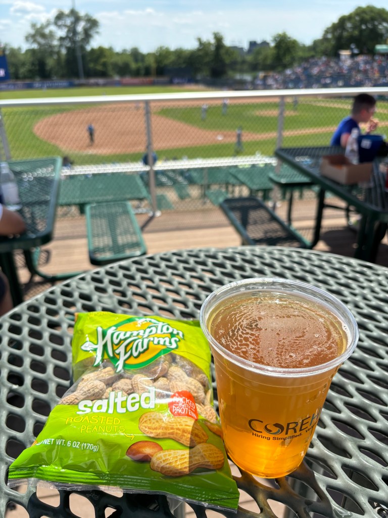 Closeup of beer and bag of peanuts with the ballfield in the background.