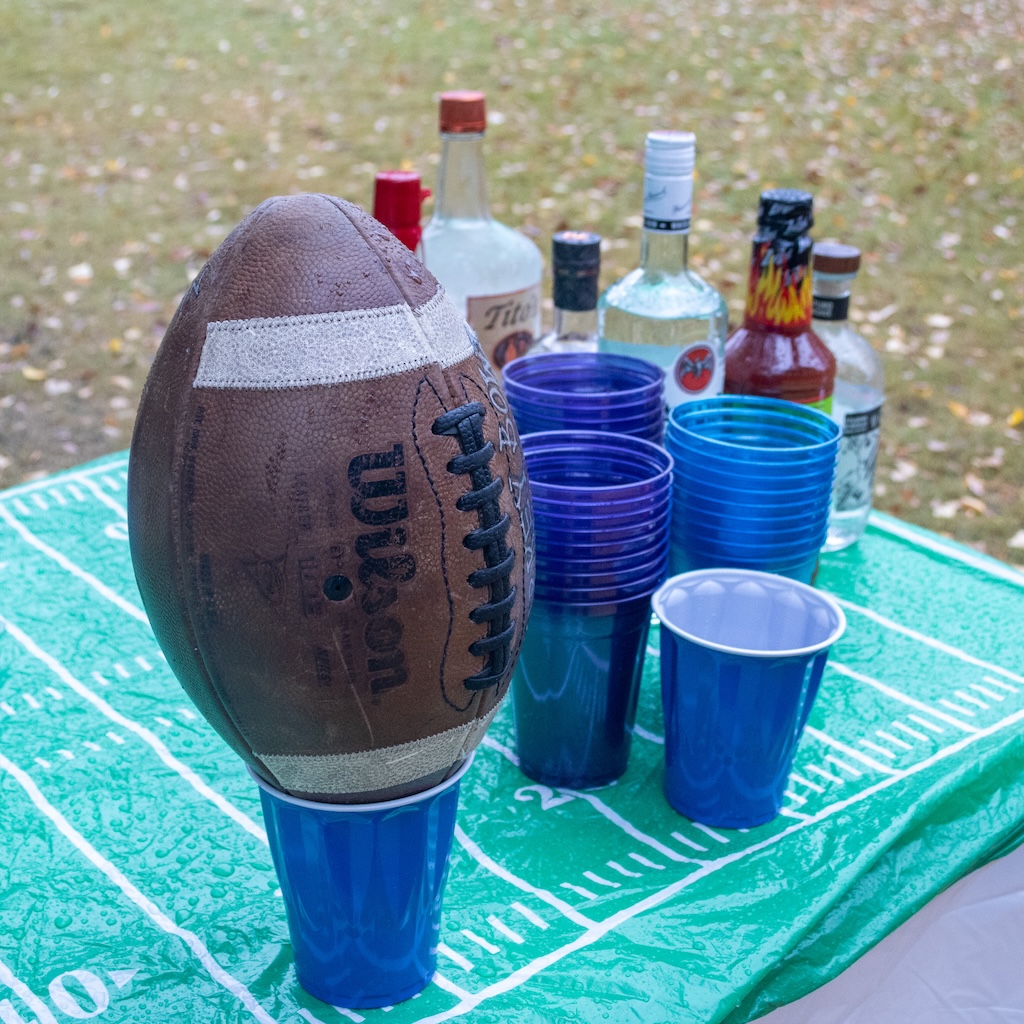 A football in a plastic cup, with booze bottles in the background.