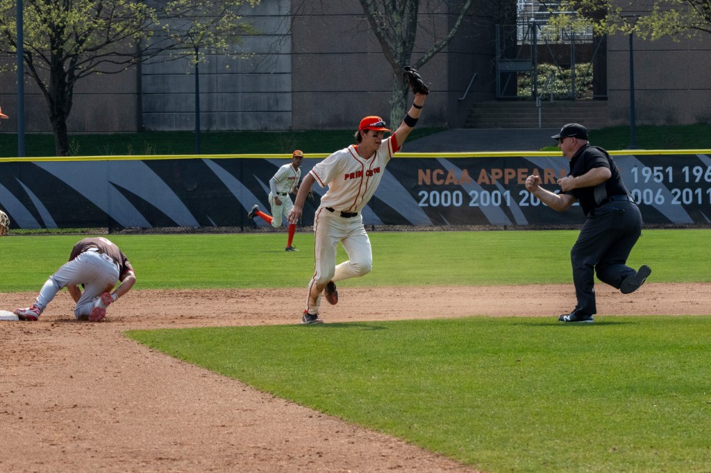 Shortstop holds ball in glove up high, while umpire signals out. Brown runner is on one knee at second.