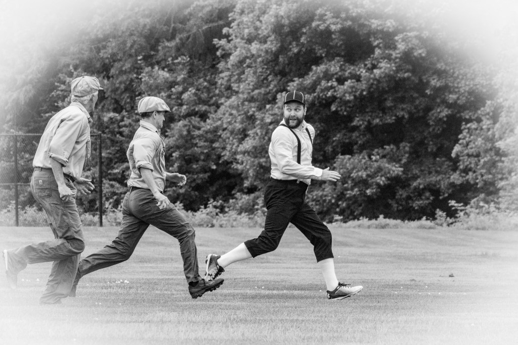 Runner heading back to first base looks back toward two fielders chasing him in rundown.