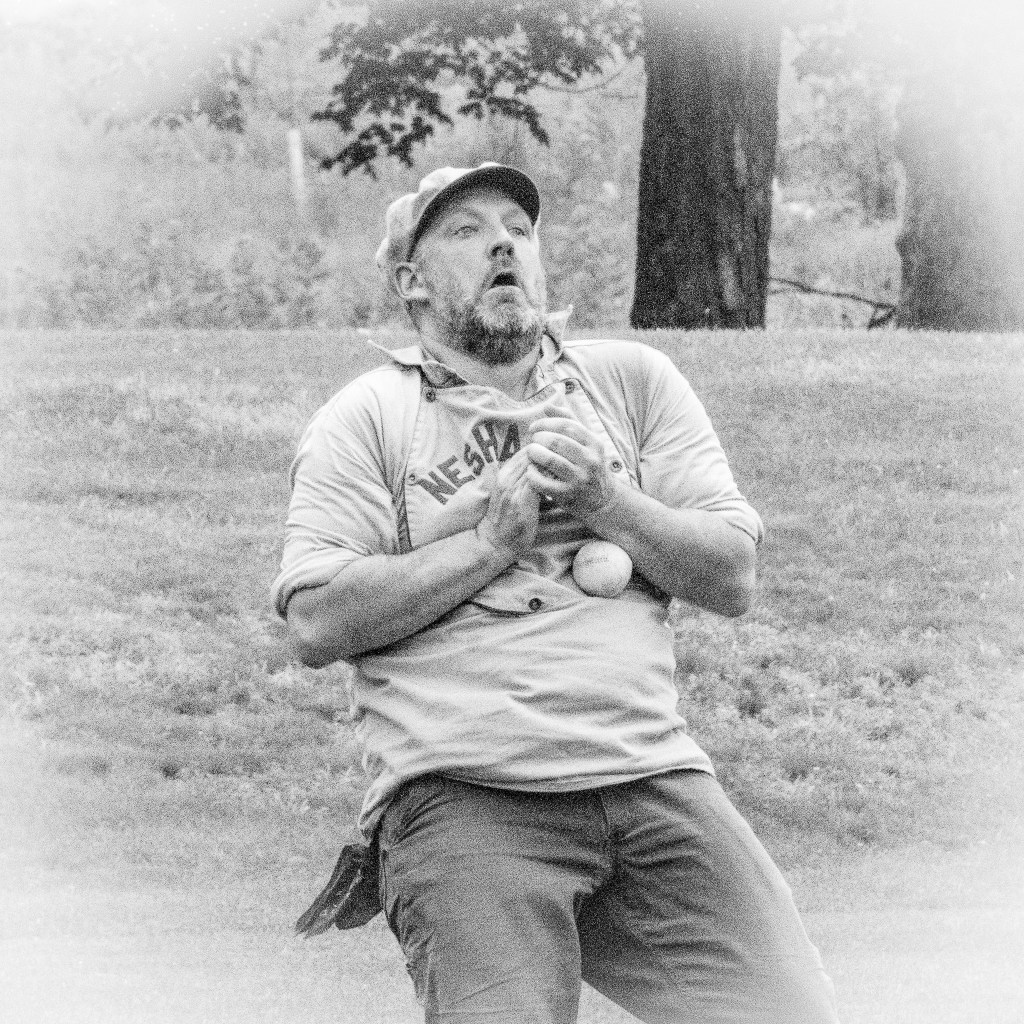 A fielder tries to grab the ball, which is tucked into his stomach by his left arm.