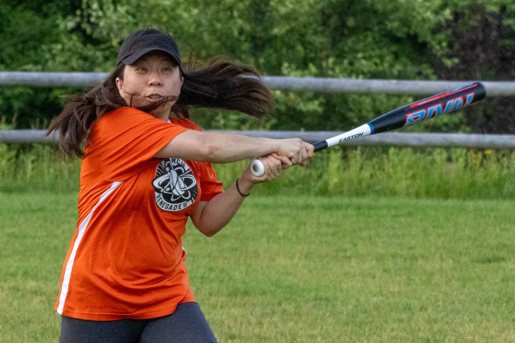 Female batter swings the bat, with her long hair flying in all directions.