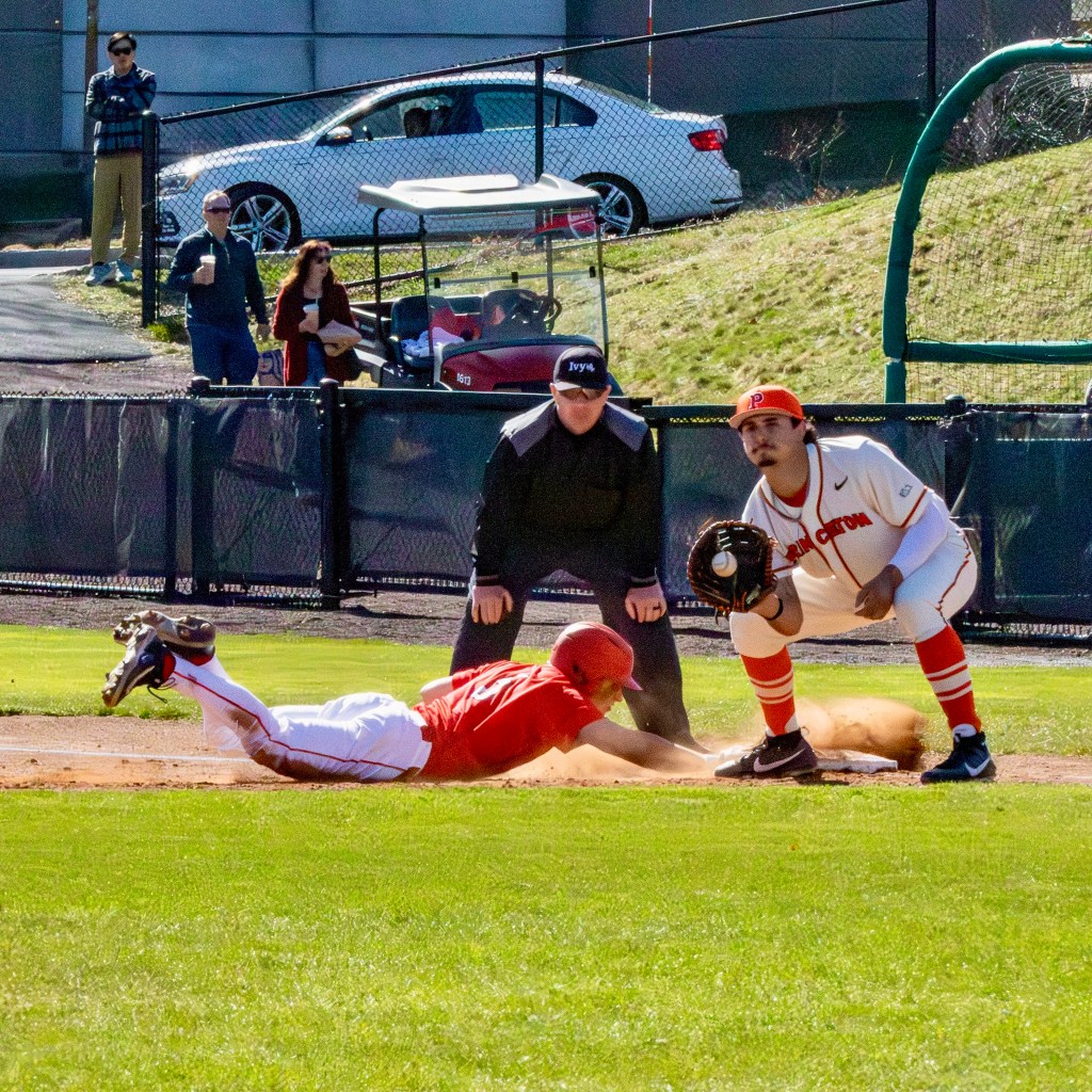 The pickoff throw pops into the open glove of the first baseman as the runner dives into the bag and raises a cloud of dirt.
