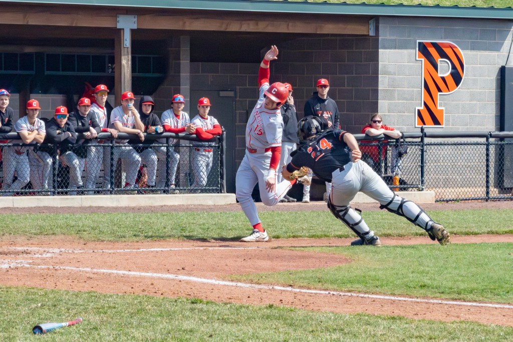 Princeton catcher stretches to apply tag to the Cornell runner arching his body to try to avoid the tag as heads toward home plate.