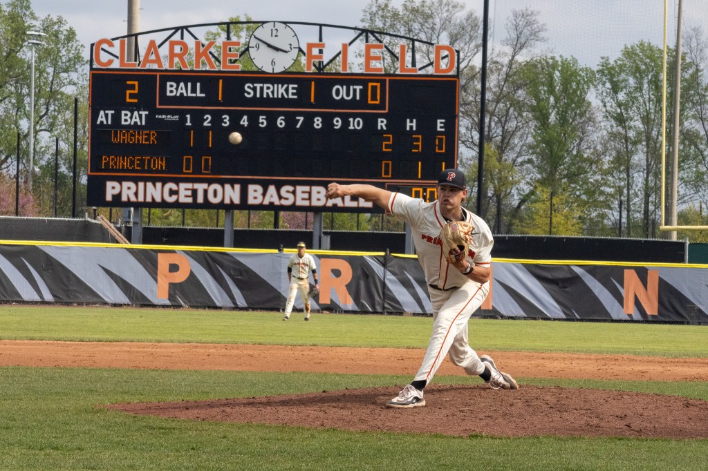 Pitcher James Beasley throws the ball toward home plate. The ball has just been released and covers the visitors' third inning run total space on the scoreboard in the background.
