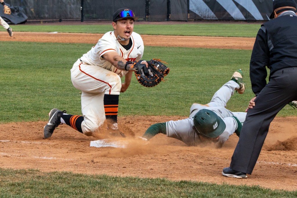 First baseman extends his glove with the ball in its pocket toward the umpire with hands on knees before signaling "out."
