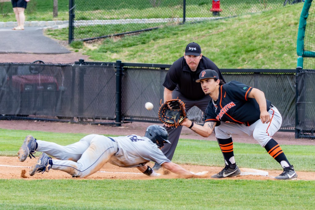 With the umpire looking on from behind, Princeton's first baseman opens his mitt to catch an approaching pickoff throw while the Yale runner dives into the bag.
